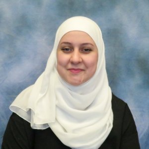 Portrait of a smiling woman wearing a white hijab and a black top posed against a blue backdrop Portrait of a smiling woman wearing a white hijab and a black top, posed against a blue backdrop.